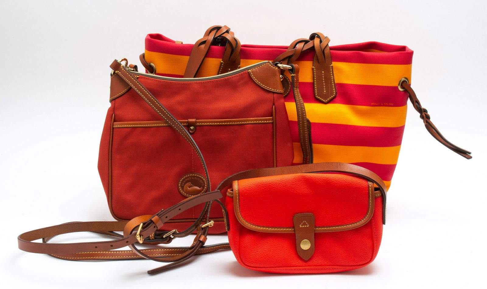 Dooney & Bourke Pink and Orange Handbags, 3: Group of three Dooney and Bourke handbags, in hues of pinks and oranges. Largest: 12” H x 12.5” W x 6.5” D.