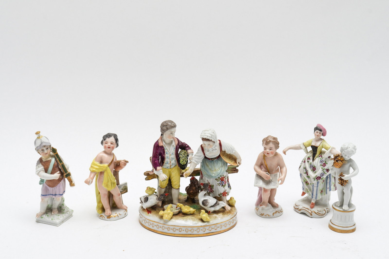 Group Of Paint Decorated Porcelain Figurines, 6: Assembled group of paint decorated figural groups, in the Continental taste, comprising a man and woman feeding geese with mark to underside for Volkstedt, a dancing lady with pink hat with blue cross