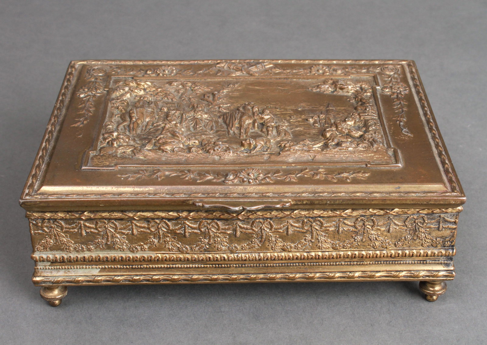 Neoclassical Manner Gilt Bronze Footed Box: Neoclassical gilt-bronze footed box with hinged lid, depicting a royal outing scene, landscape with figures, horses and dogs, marked underneath: "JB." 2.5" H x 7.5" W x 5.5" D. Heavily worn gilt, loss
