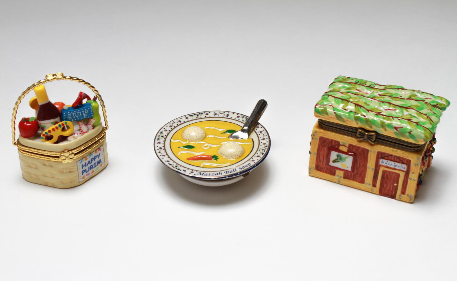 Judaica Porcelain Food-Themed Pill Boxes, 3: Three Judaica food-themed porcelain pill boxes, comprising a bowl of matzo ball soup, the box enclosing a tiny matzo ball, a "Happy Purim" basket of wine, fruits, candy, and rugelach, with gilt swing 