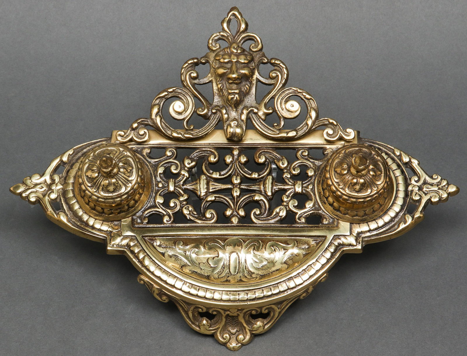 Renaissance Revival Manner Brass Inkwell: Renaissance Revival manner brass inkwell, with two ink pots flanking a smiling Grotesque mask, throughout with scrolling motifs. 3.25" H x 9.5" W x 6.5" D.