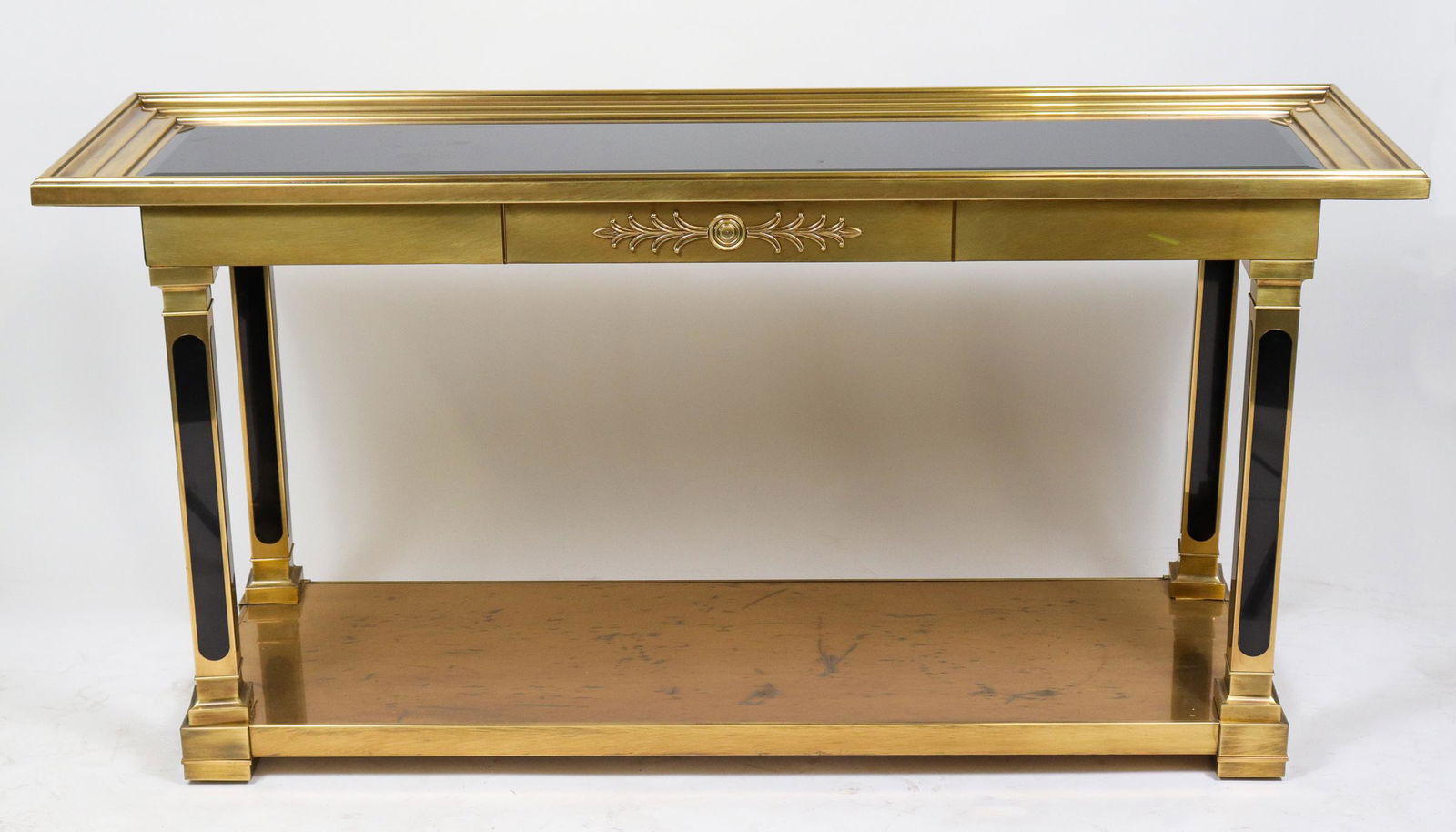 Mastercraft Style Brass & Smoky Glass Console: Hollywood Regency style in the manner of Mastercraft brass two-tier console, with a black beveled glass top, square columnar legs with lacquered panels, and neoclassical motif. 30.75" H x 62" W x 18"