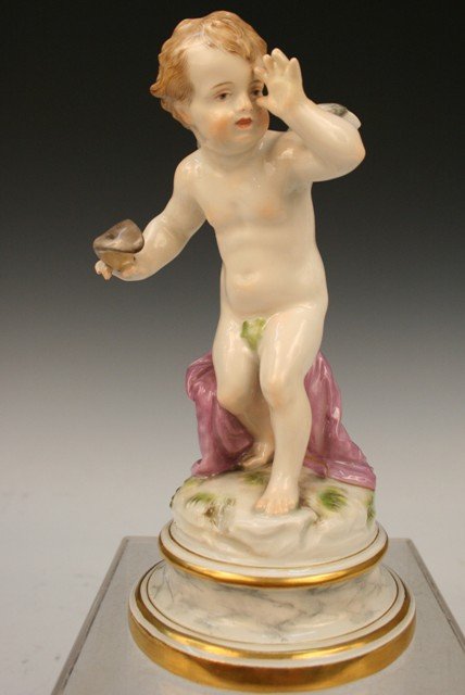 Meissen L-Series Porcelain Putto/Cupid Figure: Porcelain figure of a putto or Cupid holding a masquerade-ball mask in 1 hand while disrespectfully thumbing his nose with the other, manufactured by Meissen, Germany, c. late nineteenth or early twen