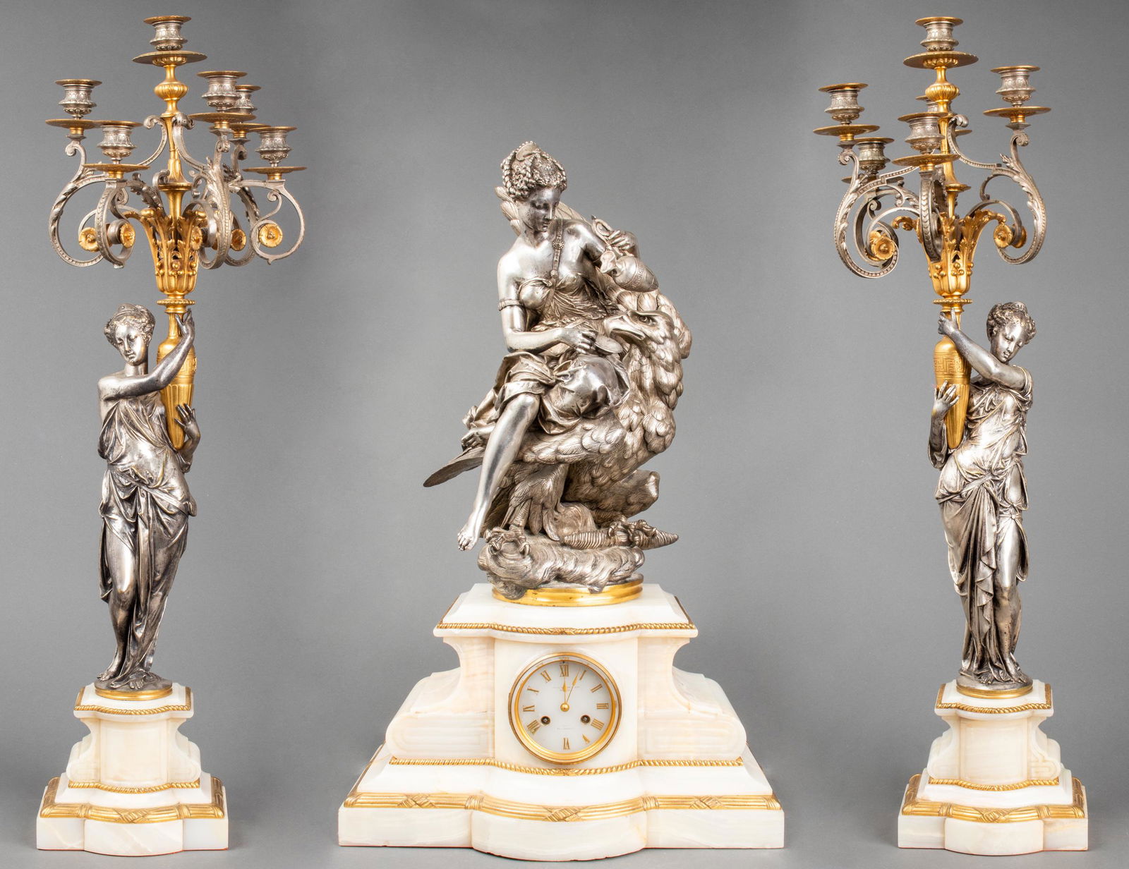 A. Carrier-Belleuse Clock & Garniture Set, 19th C.: French three-piece silvered bronze figural garniture set, the central sculpture depicting Hebe and the eagle of Jupiter, cast by Albert-Ernest Carrier-Belleuse, signed "Carrier," mounted on an onyx pl