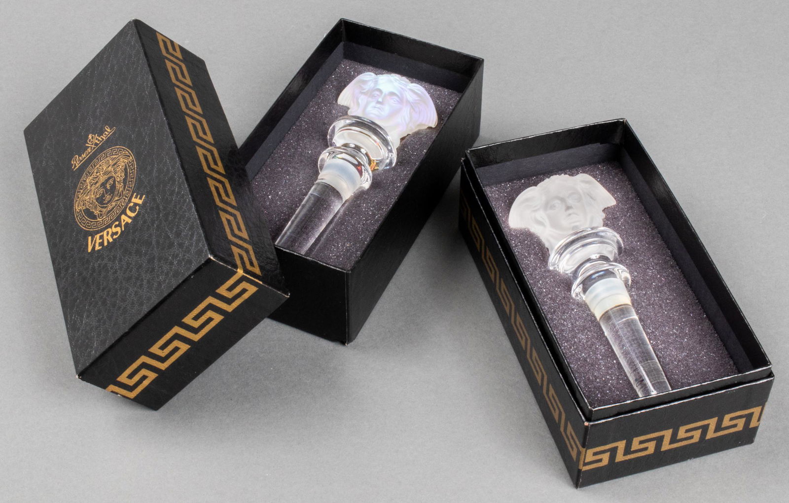 Versace Rosenthal Crystal Medusa Bottle Stoppers 2: Two Rosenthal for Versace colorless crystal Medusa wine bottle stoppers, both in original boxes, maker's mark on stem. 5" L x 2" W.