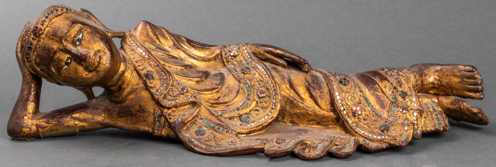 Thai Carved Giltwood Reclining Figure Sculpture: Thai carved and gilt wood sculpture of a reclining figure, with colorful applied glass disc accents highlighting the intricately rendered drapery. 6" H x 9.5" W x 8" D. Light wear commensurate with ag