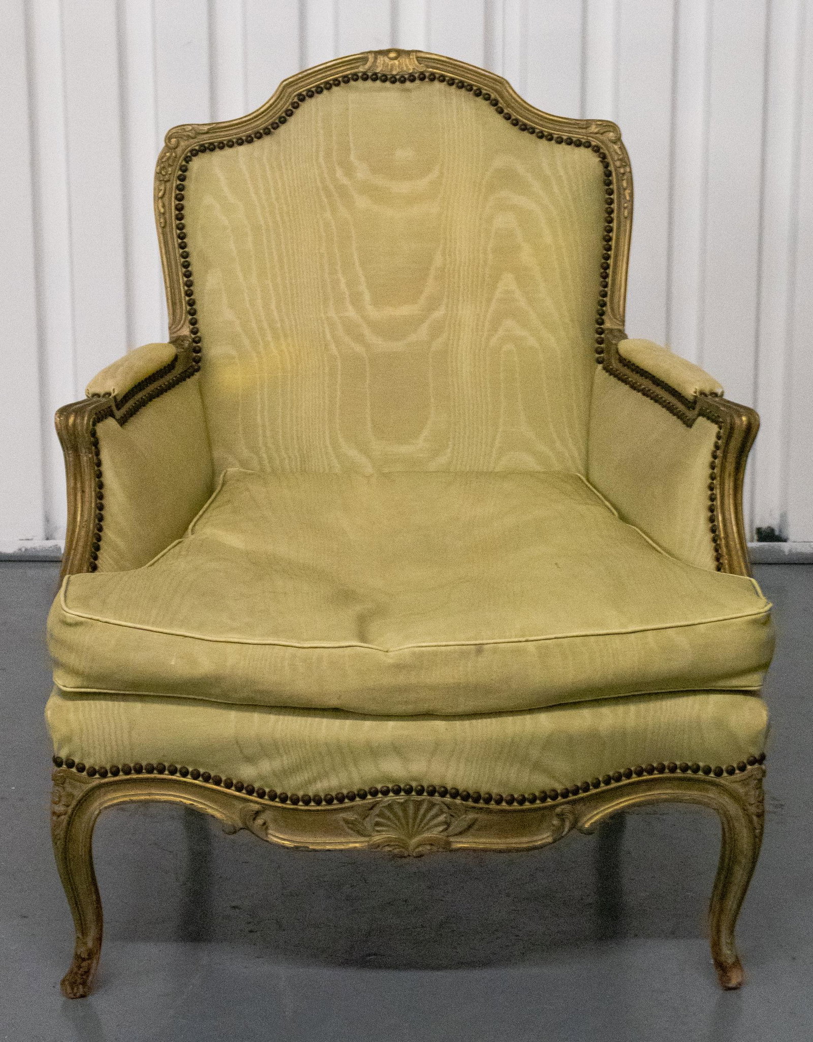 Louis XV Style Upholstered Bergère: Louis XV style upholstered bergère, the frame with scrolling details and nailhead trim around the moiré pattern fabric upholstered back and seat. 37.25” H x 30.5” W x 35” D