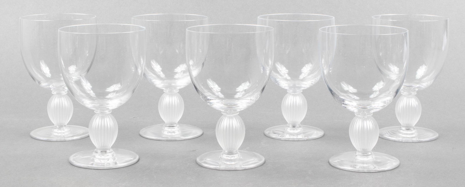 Lalique Clear Crystal Langeais Water Goblets, 7: Seven Lalique clear crystal water goblets in the Langeais pattern, each glass with wide rim and lobed stem, etched signature to base "Lalique France". 6" H x 4" diameter. Provenance: Removed from a 15