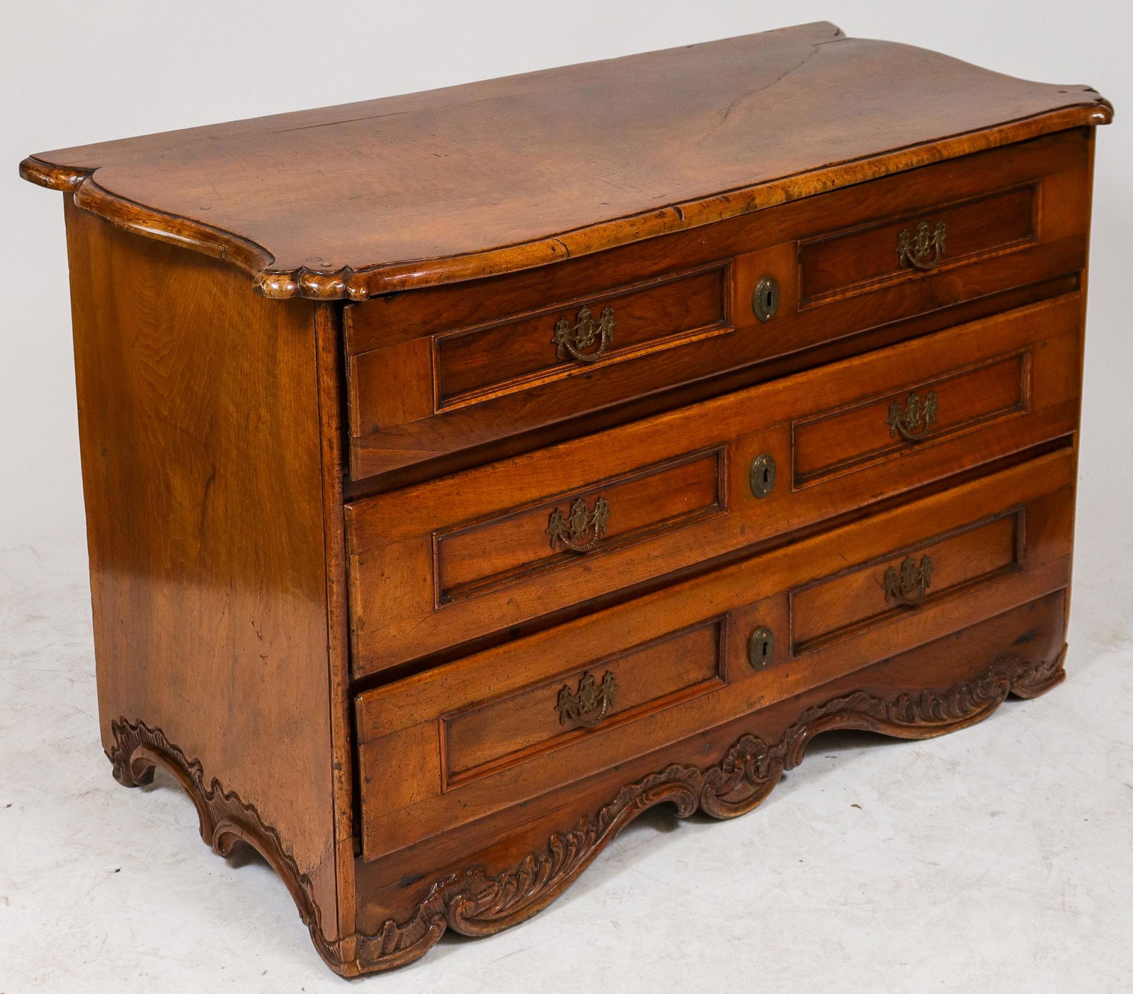 Dutch Fruitwood Commode, Antique: Antique Dutch fruitwood commode, three drawers over a carved apron base, brass swag pulls, circa late 18th century. 31" H x 48" W x 24" D. Lacking key.