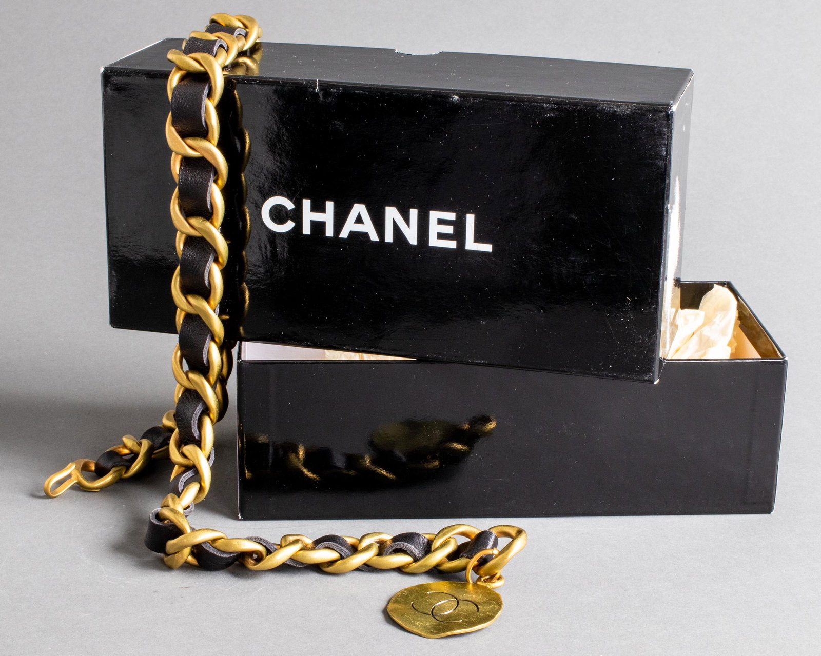 Chanel Gold-Tone Link And Black Leather Belt: Chanel gold-tone metal belt with woven black leather and medallion with interlocking "CC" logo, signed to buckle, from the 1994 Spring (Printemps) Collection, with Chanel box. 28.5" L. Provenance: Pro