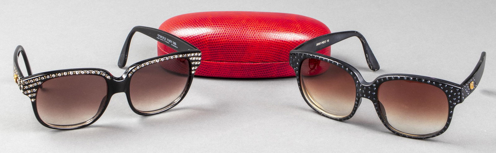 Emmanuelle Khanh Paris Designer Sunglasses, 2: Emmanuelle Khanh Paris designer sunglasses, two pairs, each featuring black tone frames with faceted rhinestones, each marked to interior, with single red embossed hard case. 2.25" H x 5.75" W x 4.75"