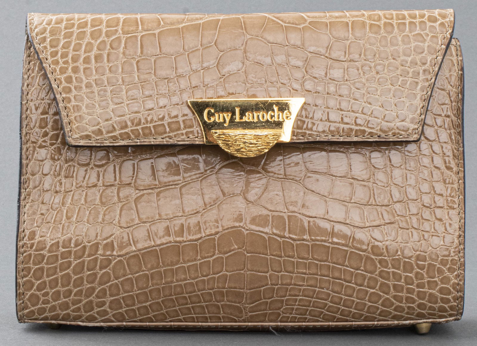 Guy Laroche Tan Alligator Handbag: Guy Laroche tan alligator clutch handbag with gold-tone hardware (lacking shoulder strap), marked "Guy Laroche" to clasp and interior. 5” H x 6.75” W x 1.5” D. Wear, interior heavily marked.