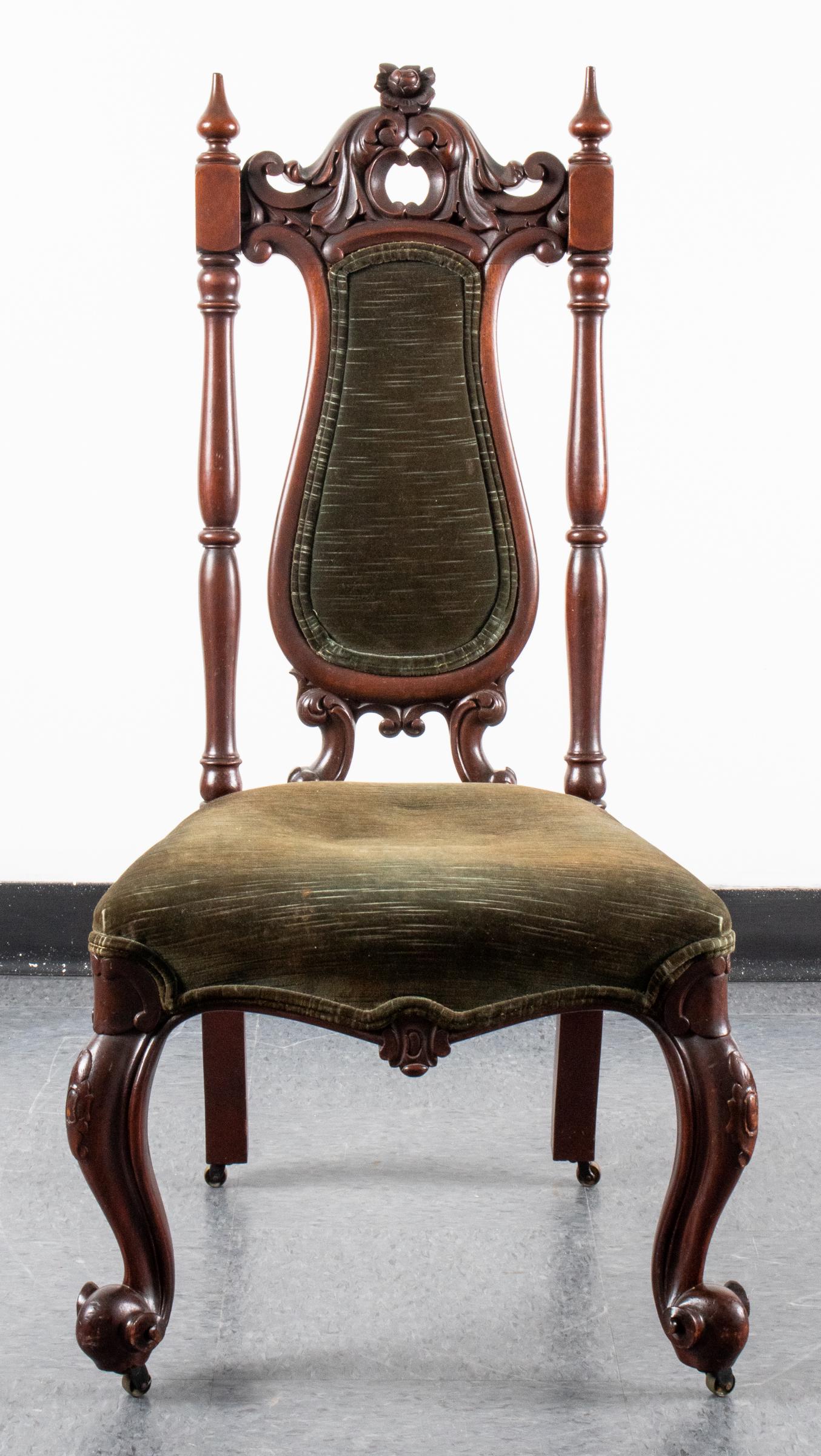 Victorian Style Carved Wood Slipper Chair: Victorian style carved low chair, with green velvet upholstered seat and back, with elaborate crest rail, the front two legs on casters. 38" H x 21" W x 20" D.