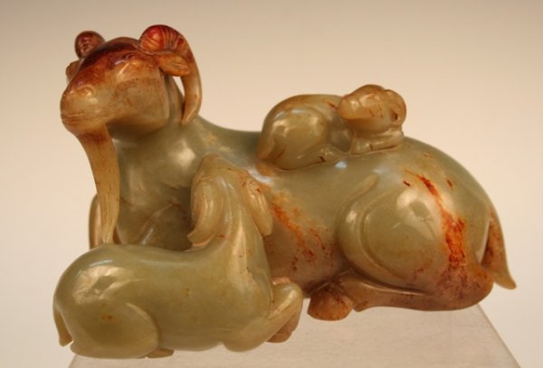 Chinese Jade Carving of 3 Rams ca. 1920s-50s: Heavy carving of three rams lying on their stomachs, one older ram with a small, young ram lying on its back and another young ram lying next to it, nuzzling his neck, with brown rusting predominantly