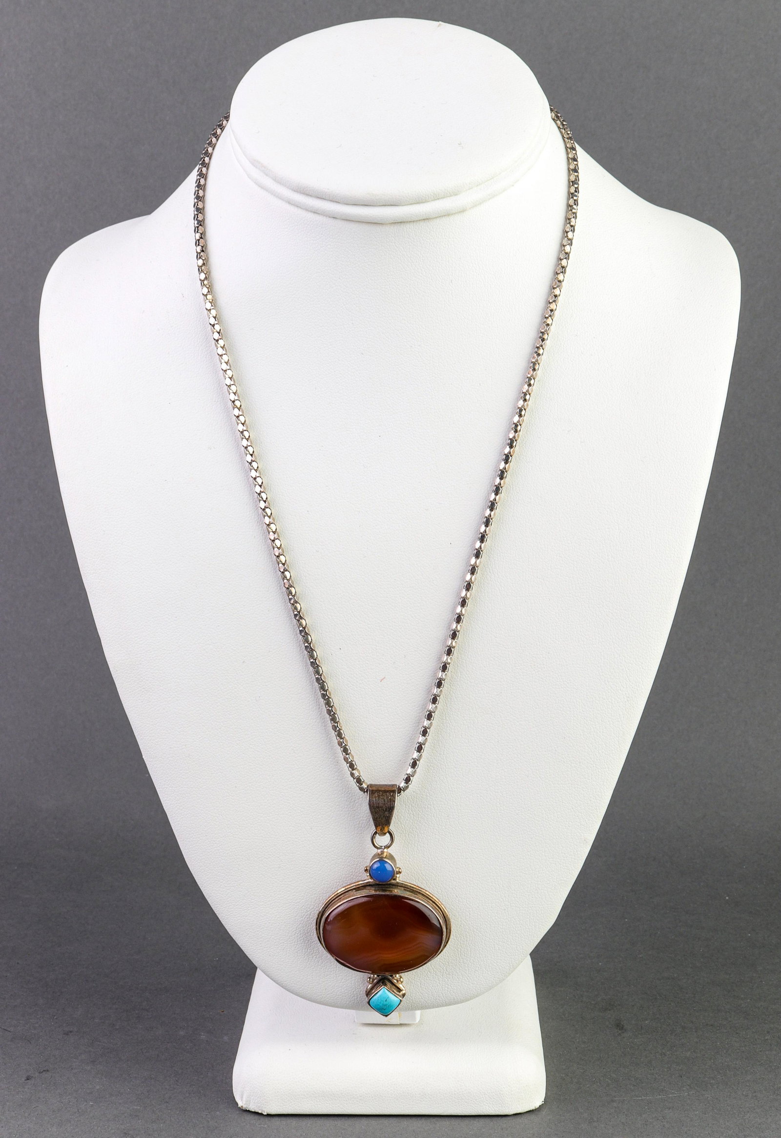 Silver, Carnelian, Turquoise & Blue Stone Necklace: Sterling silver, carnelian, turquoise and blue stone pendant necklace marked: "925 / ITALY / 1758 AR." Pendant measures: 2.375" L x 1.375" W on 21.5" L x 0.125" W popcorn chain. Oval cabochon-cut carn