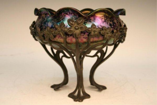 Favrile Nouveau Glass Bowl & Metal Stand: Art Nouveau iridescent favrile glass bowl featuring a folded, curving rim and etched decorations on the exterior wall, nested in a three-legged floral, nouveau stand, possibly Loetz, glass and metal, 