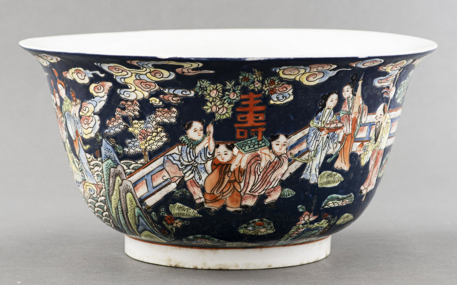 Large Chinese Canton Porcelain Bowl: Large Chinese Canton style porcelain bowl featuring celestial figures in a garden courtyard and among the waves and clouds on a deep blue ground, interior has butterflies, flowers and Buddhist wheel s