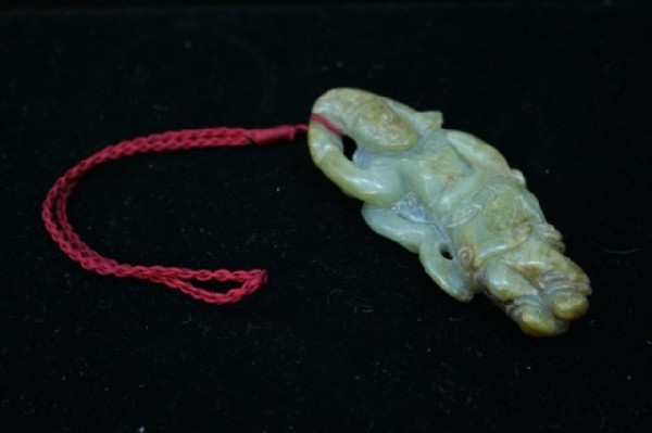 Chinese Carved Jade Figural Pendant: Carved green and brown toned jade pendant of a figure in decorated garb, China; unmarked. Dimensions: 3-1/2"L x 1-1/2"W x 1/2"D