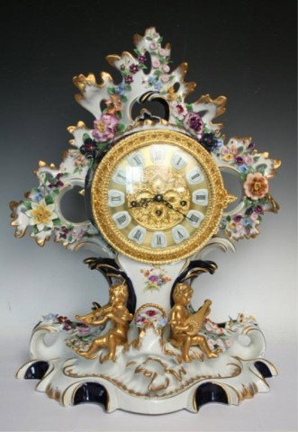 German Porcelain Gilt Nouveau Musical Angel Clock: Art Nouveau musical mantle Franz Hermle (two jewels) clock featuring two seated putti playing a violin and guitar with hand-painted and gilded decoration, delicately-rendered flower heads, accompanied