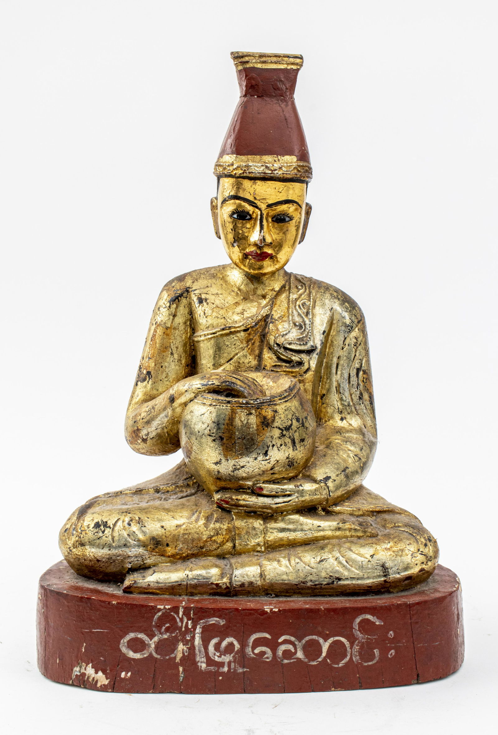 Burmese Giltwood Nat Disciple Statue: Burmese giltwood Nat disciple statue, showing a musician playing a drum, painted and gilded wood with inlaid glass eyes, script painted around the wooden base. 18.5" H x 12" W x 7.5" D