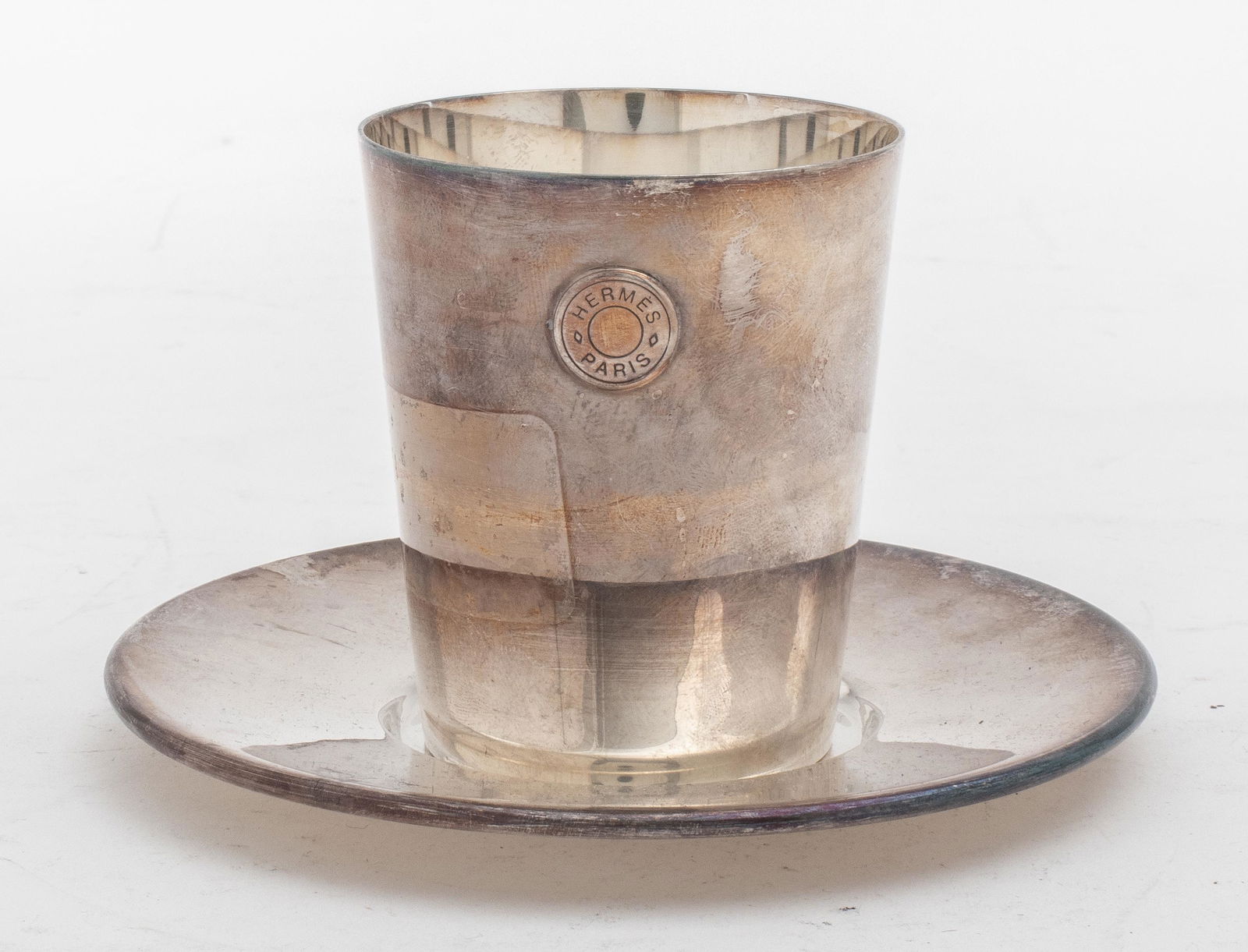 Hermes France Silverplate Beaker or Cup: A Hermes France silverplate beaker with a round underplate, marked "Hermes Paris / Made in France." The beaker 3" H x 2.5" W, the undertray 5" in diameter.