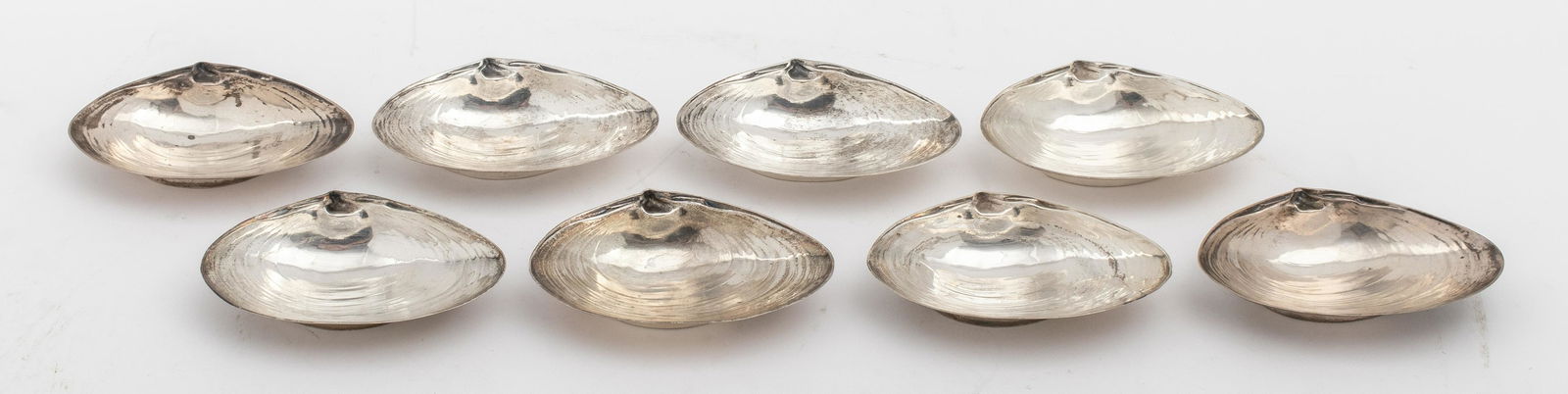 Wallace Sterling Small Clam Nut Dishes, 8: A set of 8 Wallace sterling silver nut dishes in the shape of a natural clam, marked on the reverse "Wallace / Sterling / 393." 0.5" H x 3.5" W. Weighs 7.16 ozt.