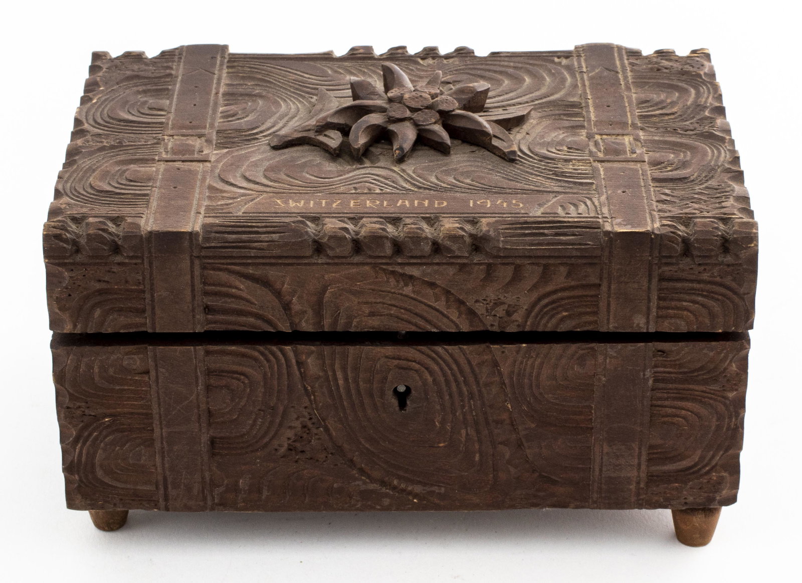 Swiss Edelweiss Carved Wood Music Box: Wooden music box decorated with an edelweiss, inscribed "Switzerland 1945," missing key. 4" H x 7" W x 4.5" D. Musical component broken and bottom cracked.