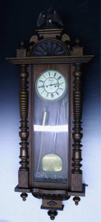 Gustav Becker Large Walnut Pendulum Wall Clock: Large walnut pendulum wall clock toped with a carved eagle, Gustav Becker (German, 1819-1995), Germany; marked. Dimensions: approx 54"H x 20-1/2"W x 8"D