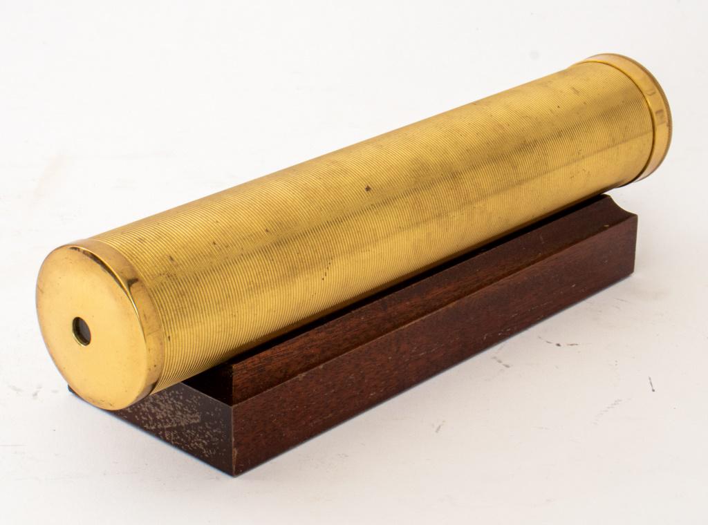 Brass and Mahogany Kaleidoscope: Brass and mahogany kaleidoscope, the tubular reeded shaft containg prisms, upon a shaped mahogany cradle. 10" L x 1.75" diameter (the kaleidoscope)
