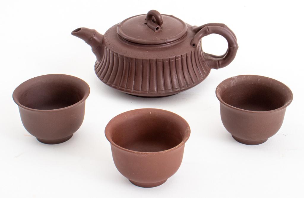 Chinese Yixing stoneware or "purpleware" lidded tea pot and three teacups, each marked to underside: Chinese Yixing stoneware or "purpleware" lidded tea pot and three teacups, each marked to underside with impressed Chinese marks, the teapot with bamboo-form handle and ribbed sides, the tea cups in t