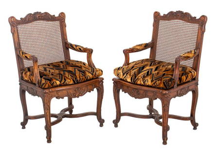 French Louis XV Style Carved Oak Armchairs, 2: French Louis XV style pair of oak armchair or fauteuil a la reine raised on cabriole legs joined by stretchers with carved shell and acanthus foliage motif to backrest and apron, having caned seat and