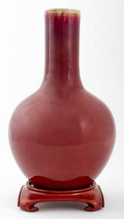 Chinese Flambe Oxblood Glazed Porcelain Vase: Chinese flambe sang de boeuf glazed ceramic porcelain vase, together with a fitted hardwood stand on four scroll feet. Vessel: 16.25" H x 10" diameter.