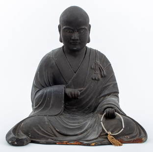 Japanese Carved Wood Arhat Figure Sculpture: Japanese, likely Meiji period (1868-1912), carved wood sculpture depicting a seated Buddhist monk or arhat with inset glass eyes and an allover textured black lacquered surface, the figure holding roc