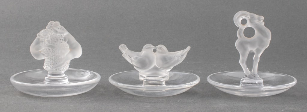 Lalique France Crystal Glass Ring Trays, 3: Three Lalique France crystal glass ring trays, one in the "Deux Colombes" pattern, one with a ram, and the third of two nude women from the Roxane collection, all marked "Lalique / France." 3.75" H x 