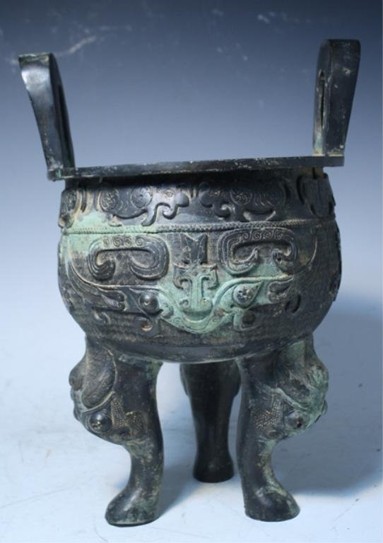 Chinese Bronze Ding Vessel Shang Dynasty: Bronze ding tripod vessel with two handles and teote mask designs, China, Shang dynasty (c. 1600-1100 BC); unmarked. Dimensions: 13-1/4"H x 8-1/2" diameter