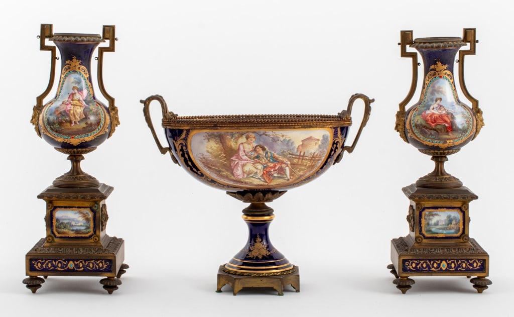 Sevres Marked Gilt Bronze Mounted Garniture Set: Sevres Marked Cobalt Blue Glazed Porcelain Garniture Set, comprising: one two-handled centerpiece bowl with hand-painted courting scenes of lovers and landscapes, and two vases with satyr mask form ha