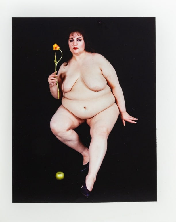 Anne Sager "Women Over 50" Photograph C-Print: Anne Sager (American, 1930-2024), "Women Over 50" Series, Color Photograph Chromogenic Print, depicting a seated nude woman upholding tulip with apple, artist's stamp verso, unframed. Image: 8.25" H x