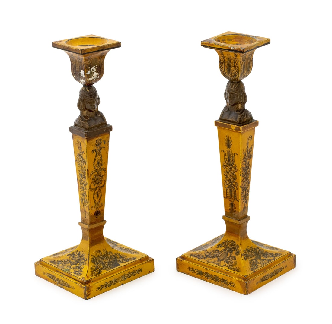 Egyptianesque Tole Peinte Candlesticks, Pair: Pair of Egyptianesque Tole Peinte Candlesticks, 19th century, each with figural busts and scrolling floral design on a yellow ground. 10" H x 3.75" W x 3.5" D. Provenance: Property from a Bunny Willia