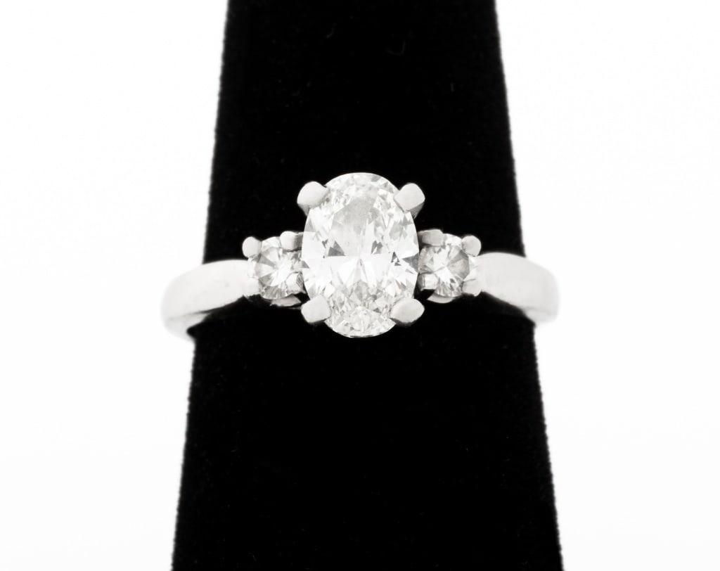 Platinum Oval Diamond Engagement Ring: Platinum Oval Diamond Engagement Ring, featuring one prong set oval brilliant cut diamond, weighing approx. 0.86 carat, F-G color / VS2 clarity, flanked by two prong set round brilliant cut diamonds