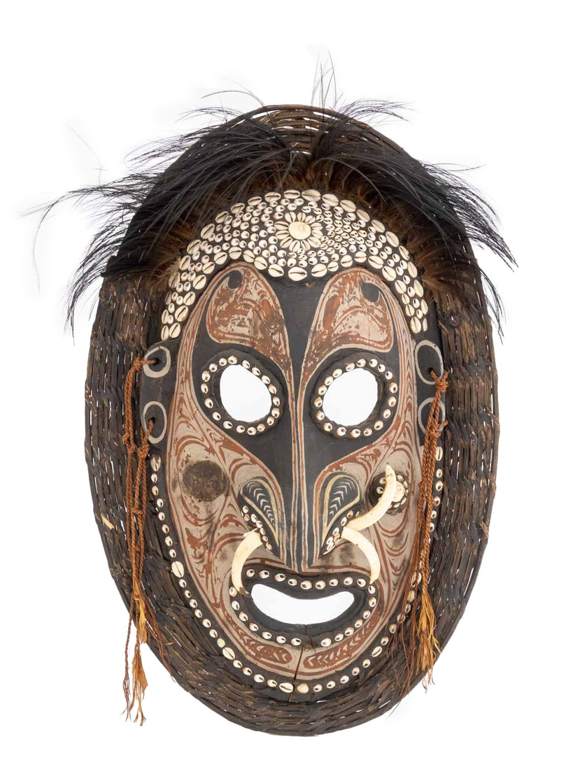Iatmul Sepik River Region Carved Wood Mask: Iatmul Sepik River Region Carved Wood Mask, cowrie shells, boar tusk nose piercing, feathered headdress, braided tassels. 26" H x 16.5" W x 5" D. Provenance: From the Collection of Laura and Lewis Kru