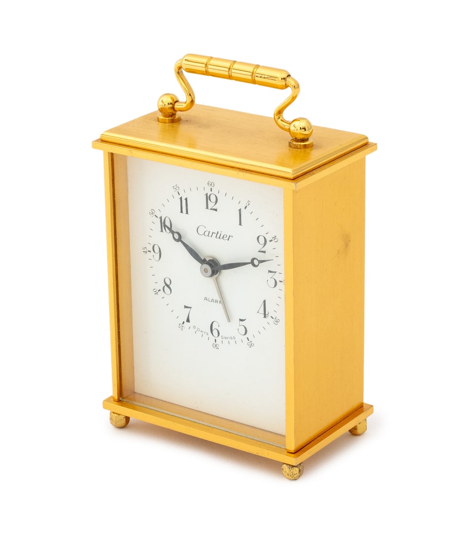 Cartier Brass Carriage Alarm Clock: Cartier Brass Alarm Clock, with white enamel clock face with Arabic numeral numbers, marked "Cartier / Alarm / 8 Days Swiss", the case with a top handle and four ball feet. 4" H x 2.5" W x 1.5" D. Pro