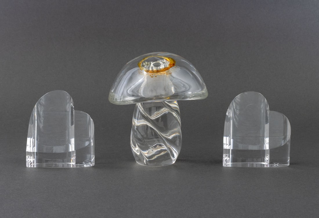 Steuben Crystal Sculptures, 3: Group of Three Steuben Crystal Sculptures, all marked to undersides and comprising: a mushroom ornament with twisted stem and a pair of flat heart paperweights. Largest: 6" H x 5.5" W x 5" D. Provenan