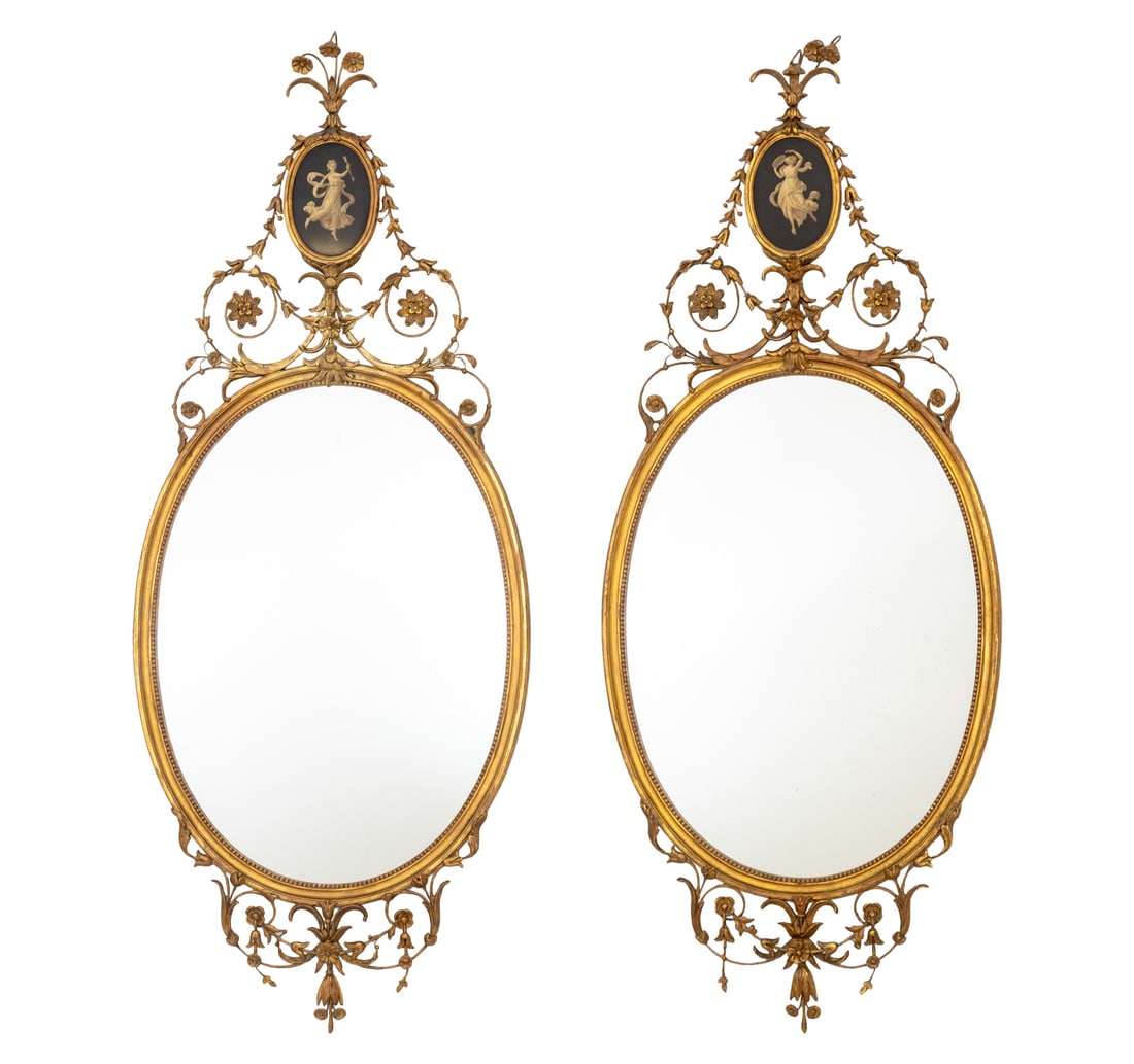 Adam Style Giltwood Oval Mirrors, Pair: Pair of Adam Style Giltwood Framed Oval Mirrors, each with gilt metal scrollwork above and below and surmounted by a hand-painted figural vignette. Overall: 49.5" H x 19.75" W x 1" D. Provenance: From