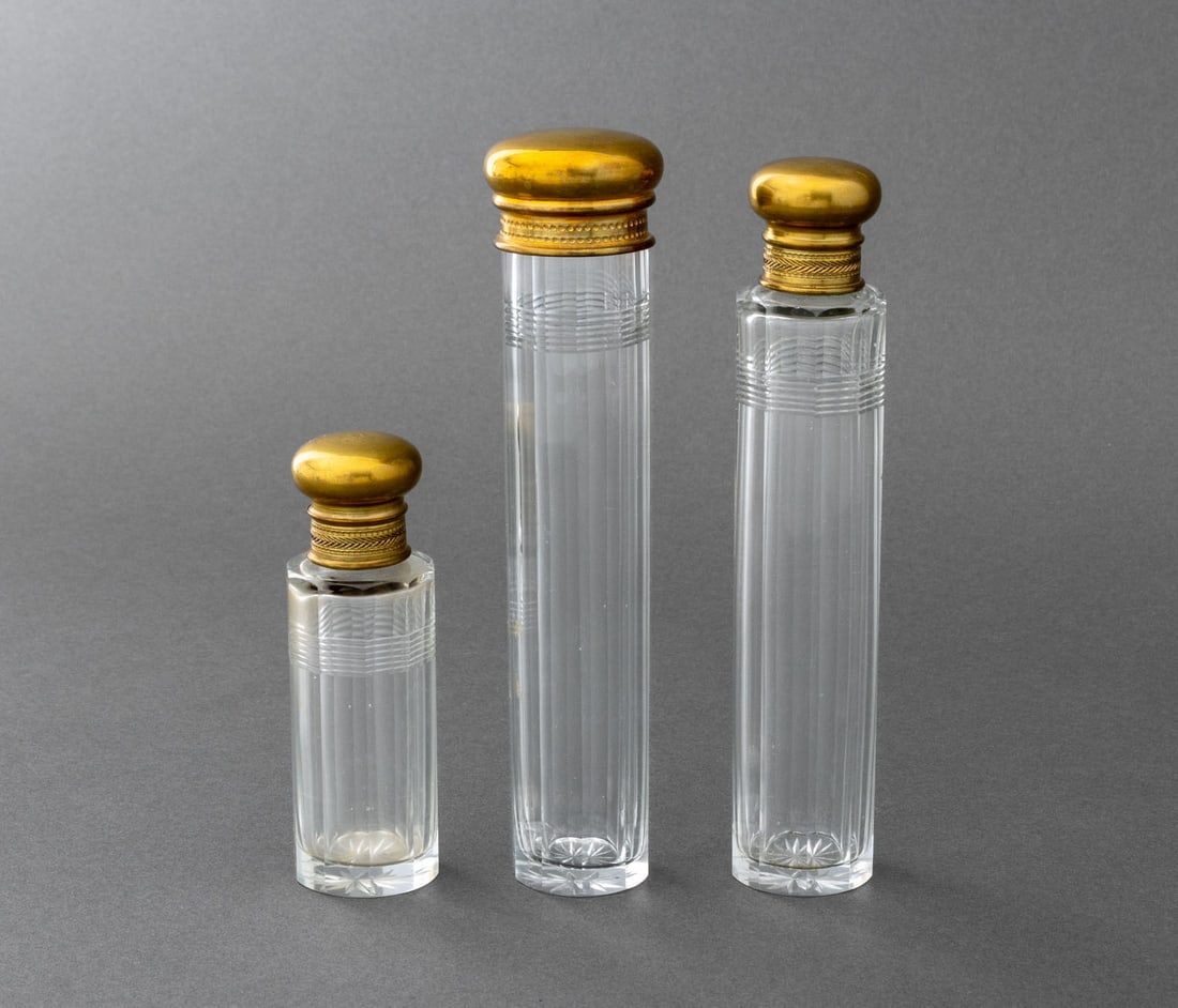 Art Deco Cut Crystal Perfume Bottles, 3: Three Art Deco Cut Crystal Perfume Bottles, each octagonal body with stopper and circular gilt metal lid, unmarked. Tallest: 7" H x 1.5" Diameter. Provenance: Property from a Bunny Williams decorated