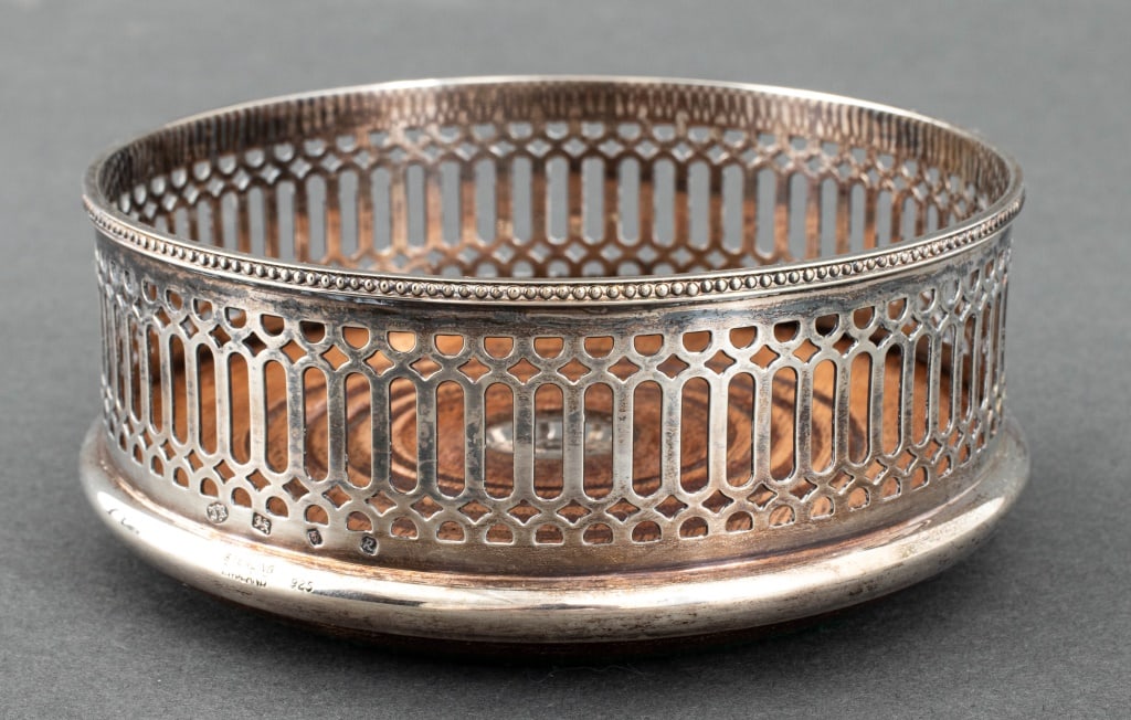 Elizabeth II Sterling Silver Bottle Coaster: Elizabeth II Sterling Silver Wine Bottle Coaster, struck with marks for James Robinson, Inc., London, 1991, and "Sterling / England / 925" near base. Weight: 5.64 ozt. inclusive; 2.25" H x 5.25" Diame