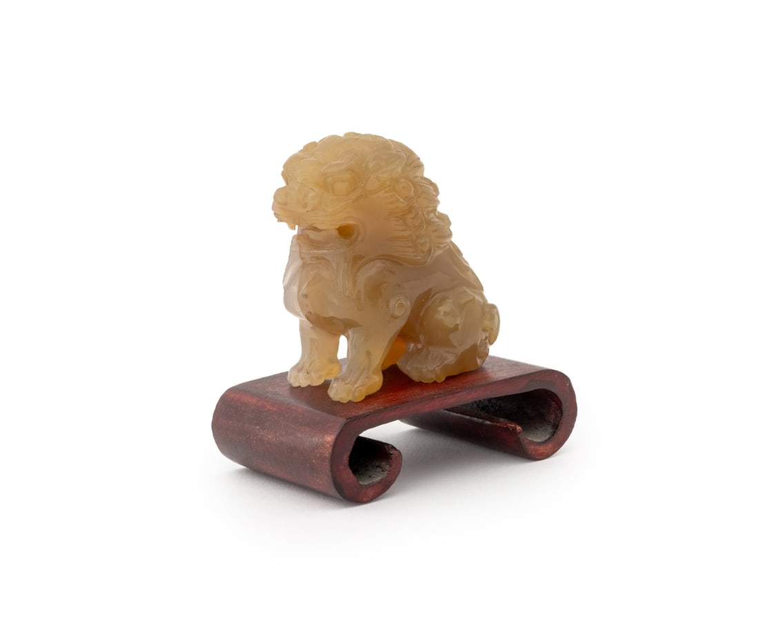 Chinese Carved Agate Buddhistic Lion Sculpture: Chinese Carved Agate Buddhistic Lion Sculpture, with a wood scroll form base. Overall: 2.5" H x 2.25" W x 1.75" D. Provenance: From a New York City Estate. Keywords: Asian Art, China, Carvings, Statue