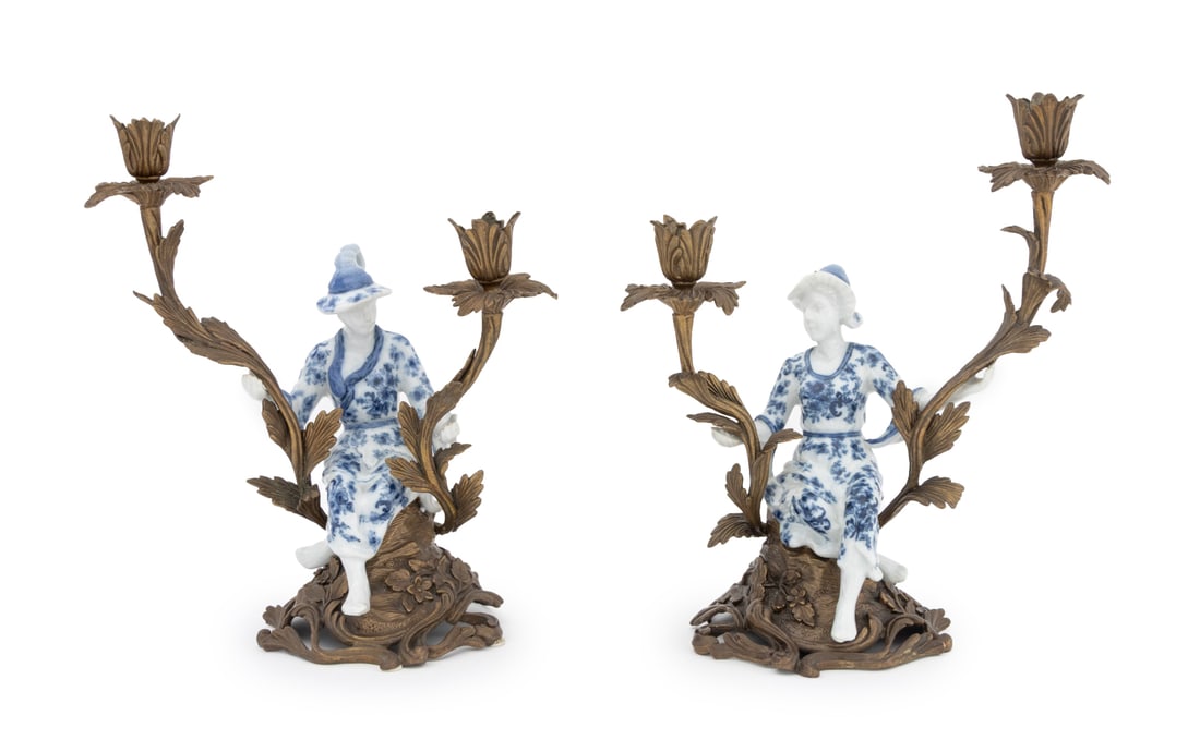 Chinoiserie Porcelain and Brass Candlesticks, Pair: Pair of Chinoiserie Porcelain and Brass Figural Two Light Candlesticks, each with blue and white porcelain figure seated on floral base. 12.5" H x 11.25" W x 7.25" D. Provenance: From an East 74th