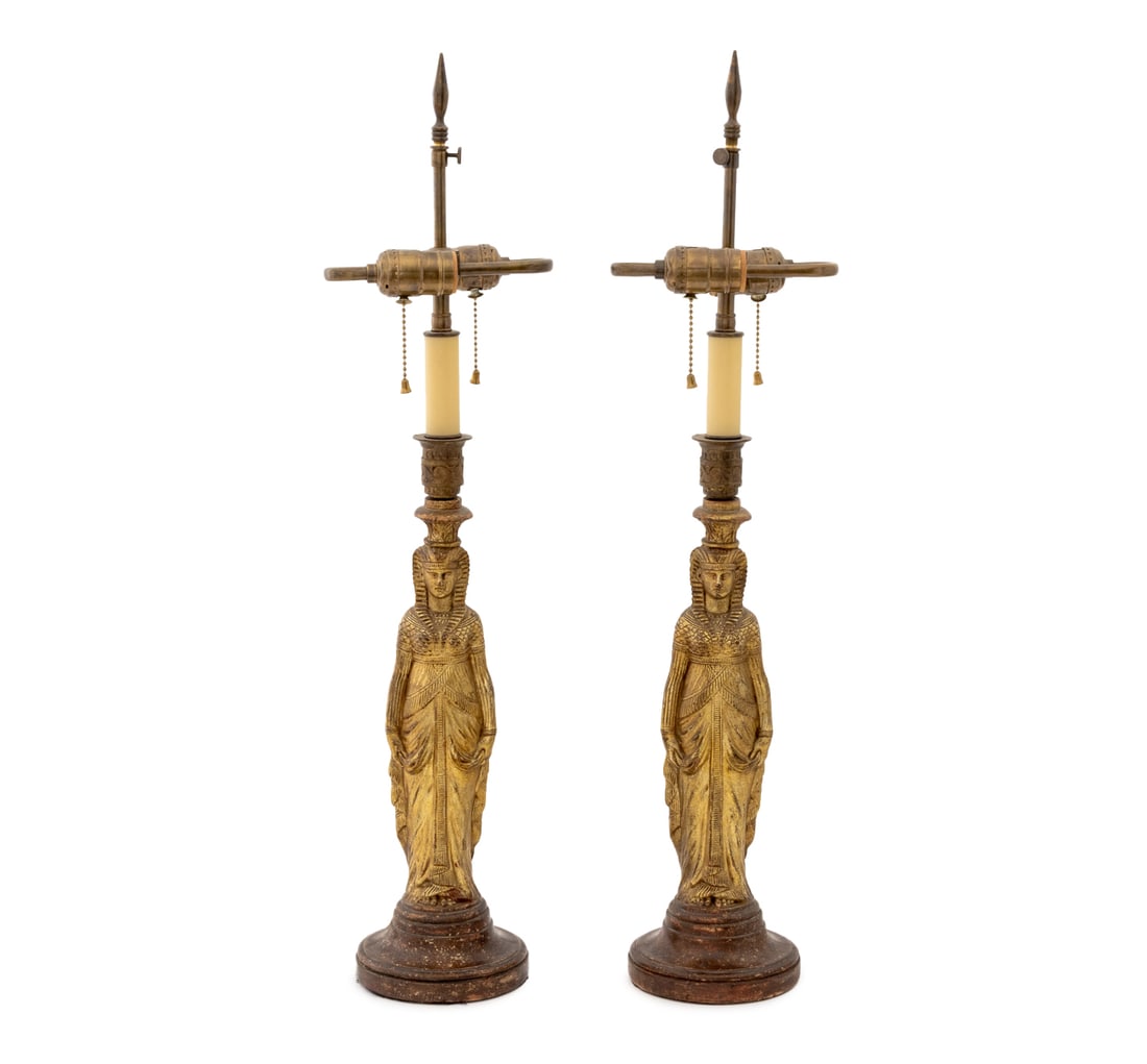 Egyptianesque Candlesticks as Lamps, Pair: Pair of Egyptianesque Figural Gilt Resin Candlesticks Mounted as Table Lamps, each atop a faux porphyry circular base with two bulb fittings. 28" H x 7" W x 6" D. Provenance: Property from a Bunny Wil