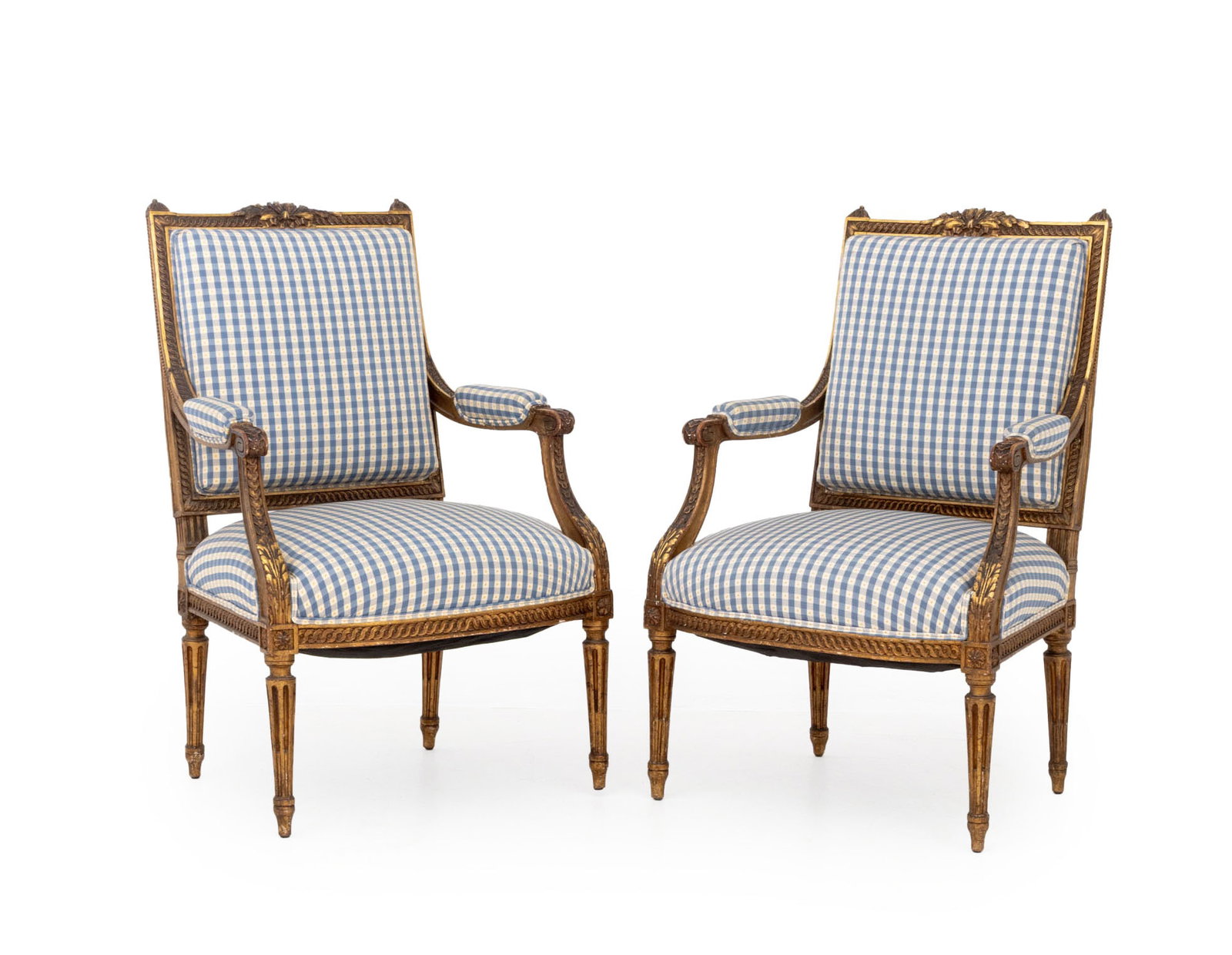 Louis XVI Style Giltwood Fauteuils, Pair: Pair of Louis XVI Style Giltwood Fauteuils, each with foliate crest, fluted legs, and upholstered in blue gingham print fabric to seat, back, and arms. 38.5" H x 25" W x 22" D; seat: 18" H. Provenance