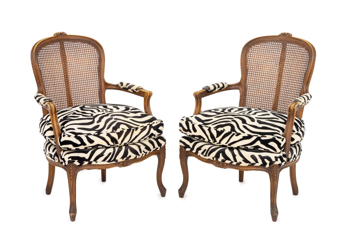 French Zebra Print Upholstered Fauteuils, 2: Pair of French Provincial Style Zebra Print Upholstered Fauteuils, each walnut frame with floral crest above a caned back and black and white zebra upholstery on four cabriole legs. 37" H x 26.5" W x